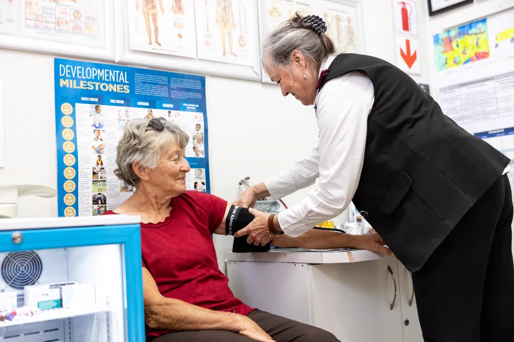 A nursing sister fitting a blood-pressure cuff to a seated patient in the clinic room