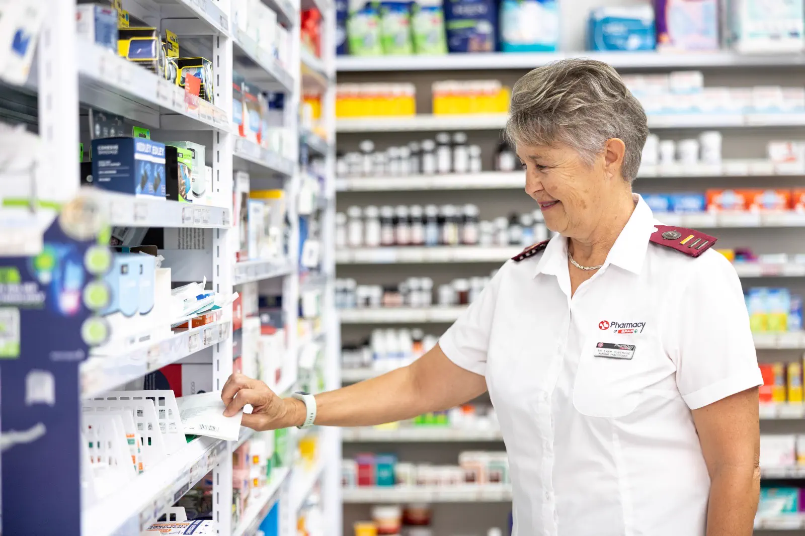 A nursing sister taking a box down from the stocked shelves in the front shop at Albertyn Pharmacy